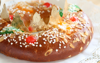 Imagen de un tradicional Roscón de Reyes español, un pan dulce circular adornado con frutas confitadas y frutos secos, representando una corona, sobre una mesa festiva