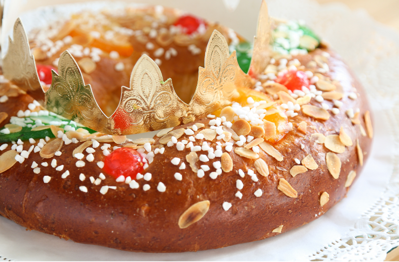 Imagen de un tradicional Roscón de Reyes español, un pan dulce circular adornado con frutas confitadas y frutos secos, representando una corona, sobre una mesa festiva